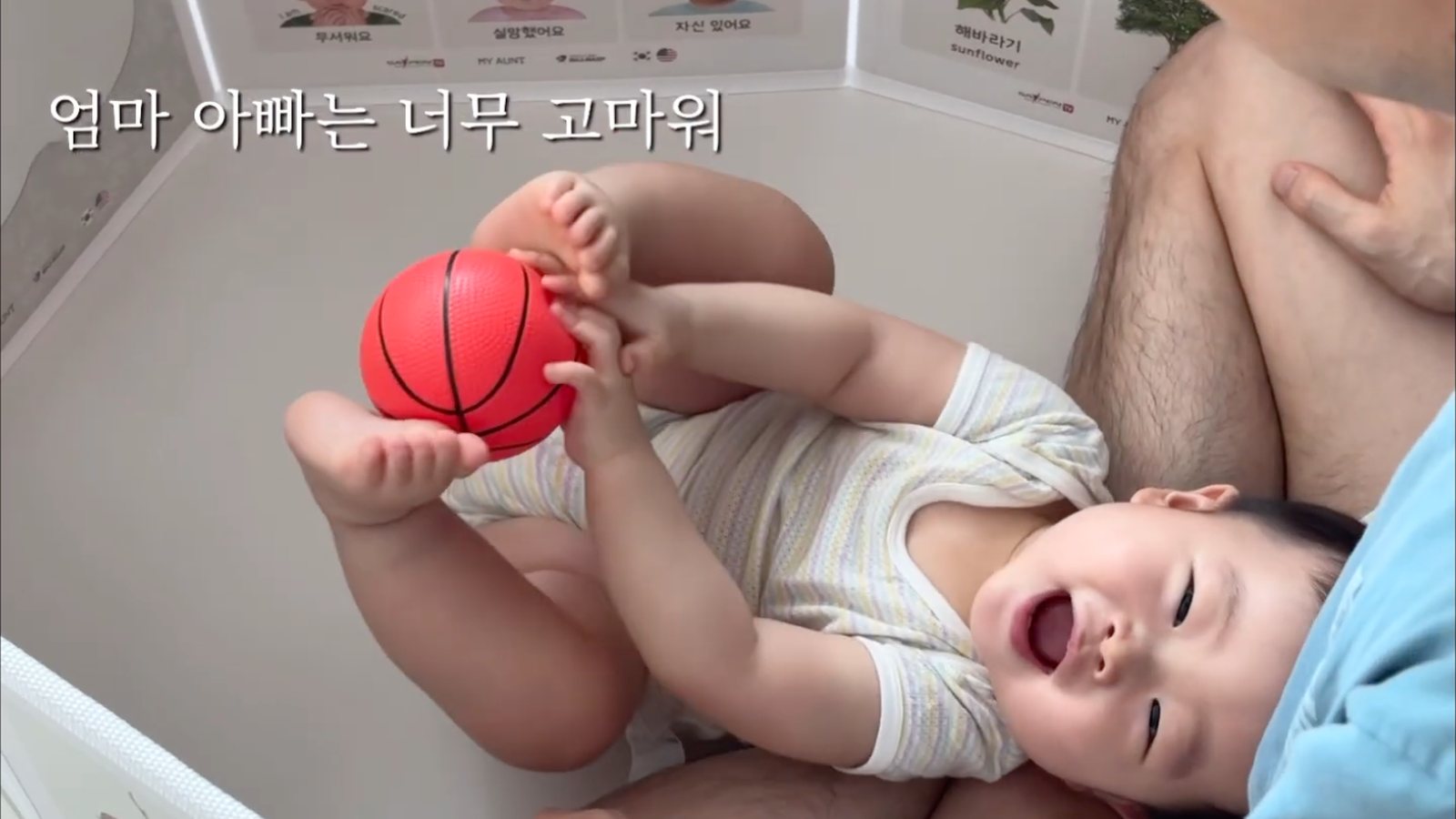 셀프 돌성장영상 장면 — 아빠 품에서 공을 가지고 노는 아기